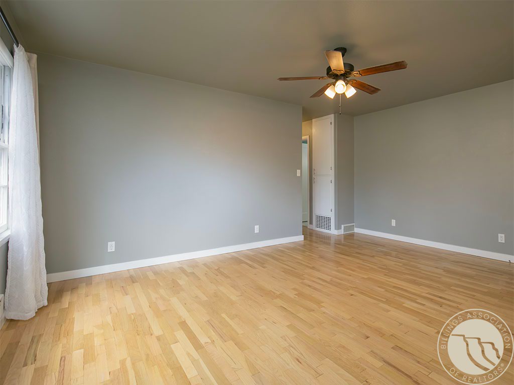 Empty room with light hardwood floors, gray walls, and a ceiling fan with lights.