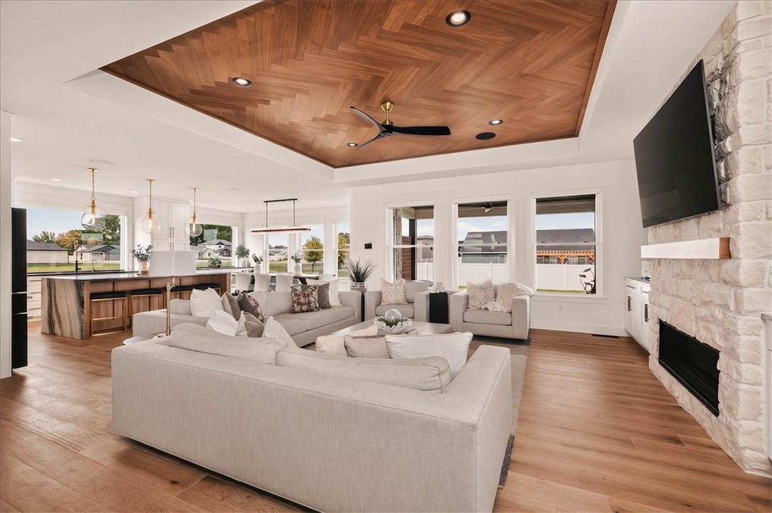 Open-plan living room with white sectional, wood-paneled ceiling, and stone fireplace.