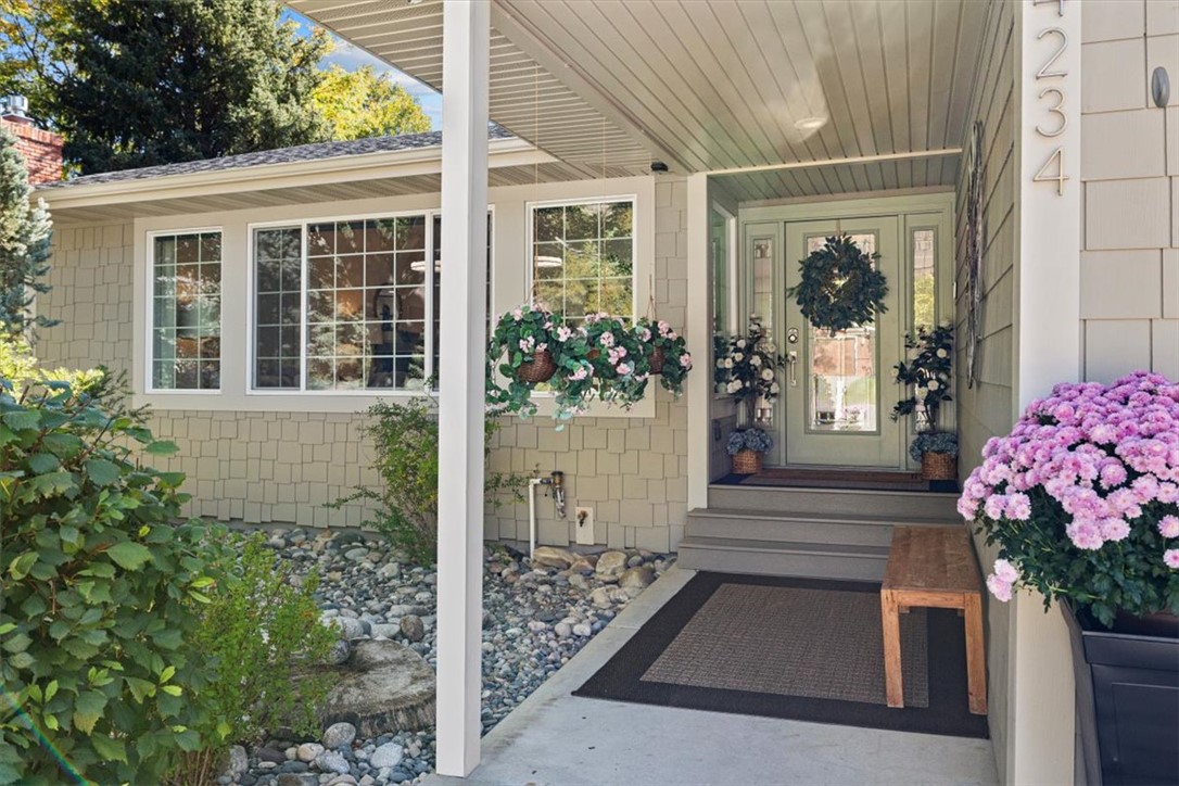 Covered front porch with a pale green glass-panel door, hanging flower baskets, and stone landscaping.