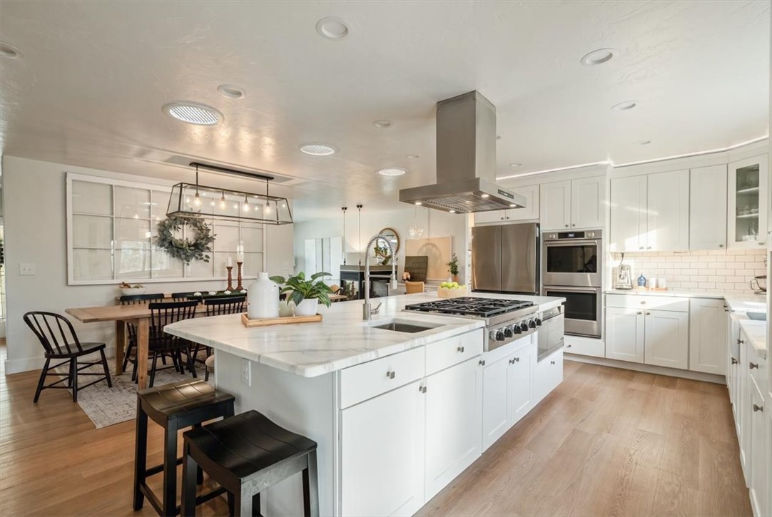 Bright kitchen with a large marble island, white cabinetry, stainless appliances, and an adjoining dining area.