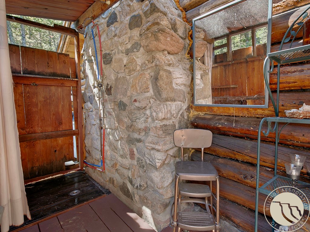 Rustic bathroom with a stone shower enclosure, exposed pipes, weathered wood walls, and a large mirror.