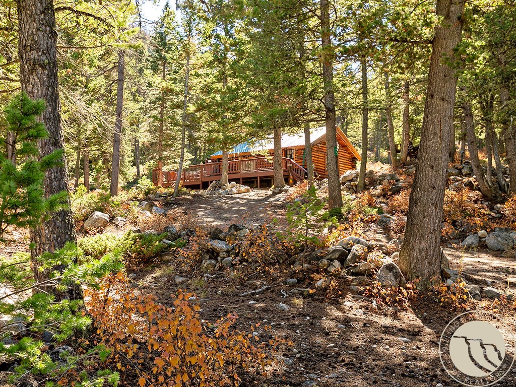 Log cabin with a broad deck sits among rocky terrain and mature forest.