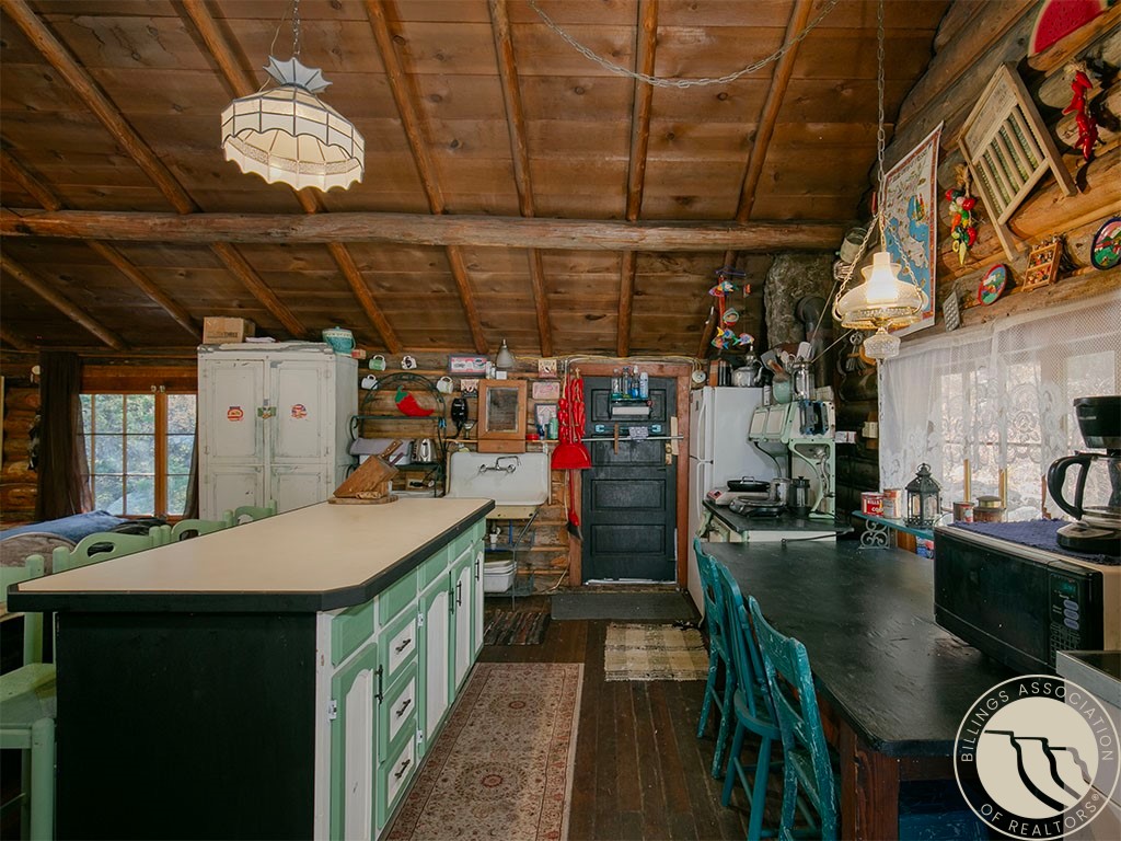 Rustic log-home kitchen with mint-green cabinets, a long island, and exposed wood ceiling.