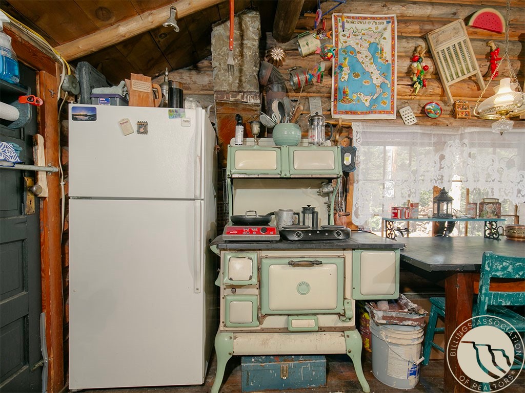 Rustic log-cabin kitchen with a mint-green vintage stove, white refrigerator, and lace-curtained window.