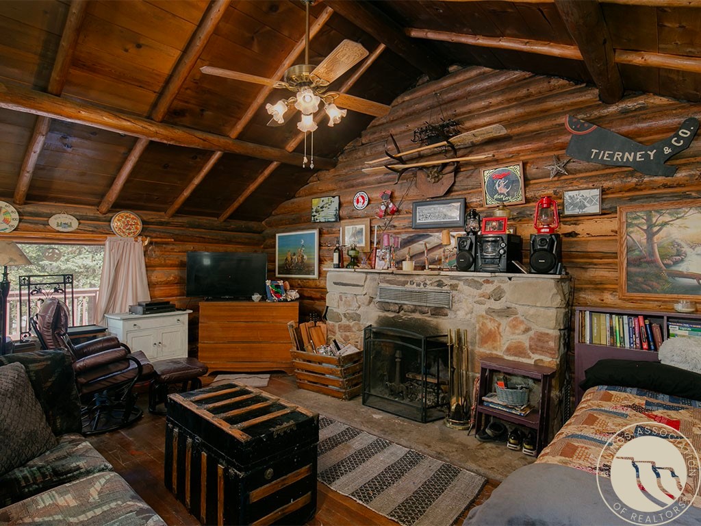 Rustic log-cabin living room with a stone fireplace, exposed beams, leather seating, and a wood-burning stove.