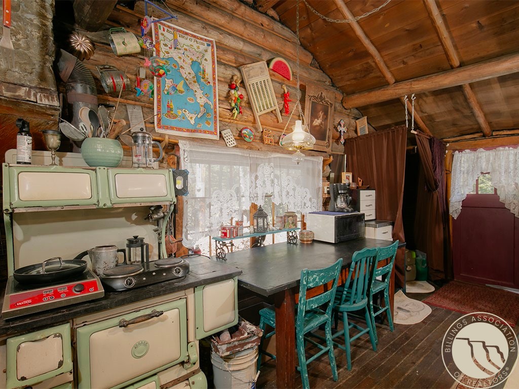 Rustic kitchen with a vintage green stove, exposed timber ceiling, and turquoise chairs around a long table.