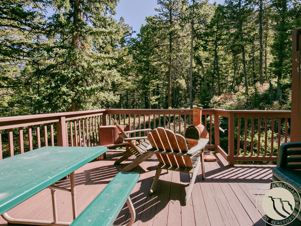Wooded outdoor deck with Adirondack chairs, a picnic table, and reddish-brown railings.