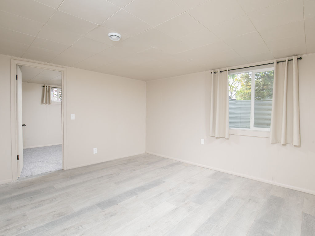 Empty room with light gray plank flooring and a curtained window.