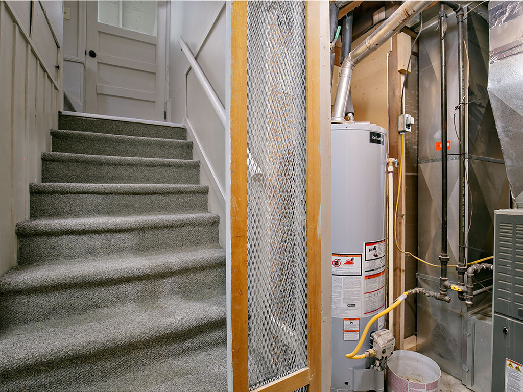 Basement stairs beside a utility area with a Rheem water heater and exposed furnace equipment.