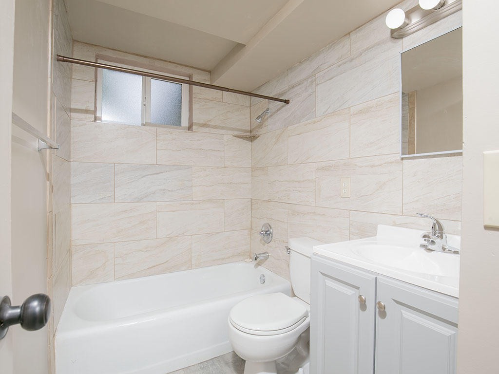 Bathroom with a white tub, toilet, and vanity against beige tiled walls.