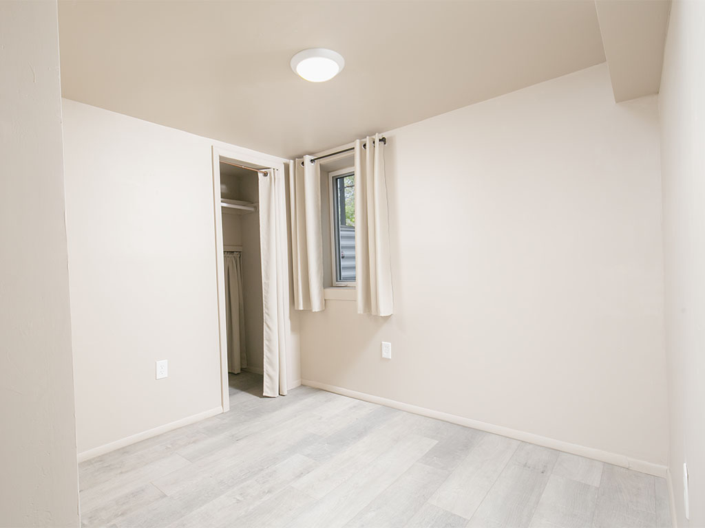 Vacant bedroom with light gray plank flooring, a curtained window, and an open closet.