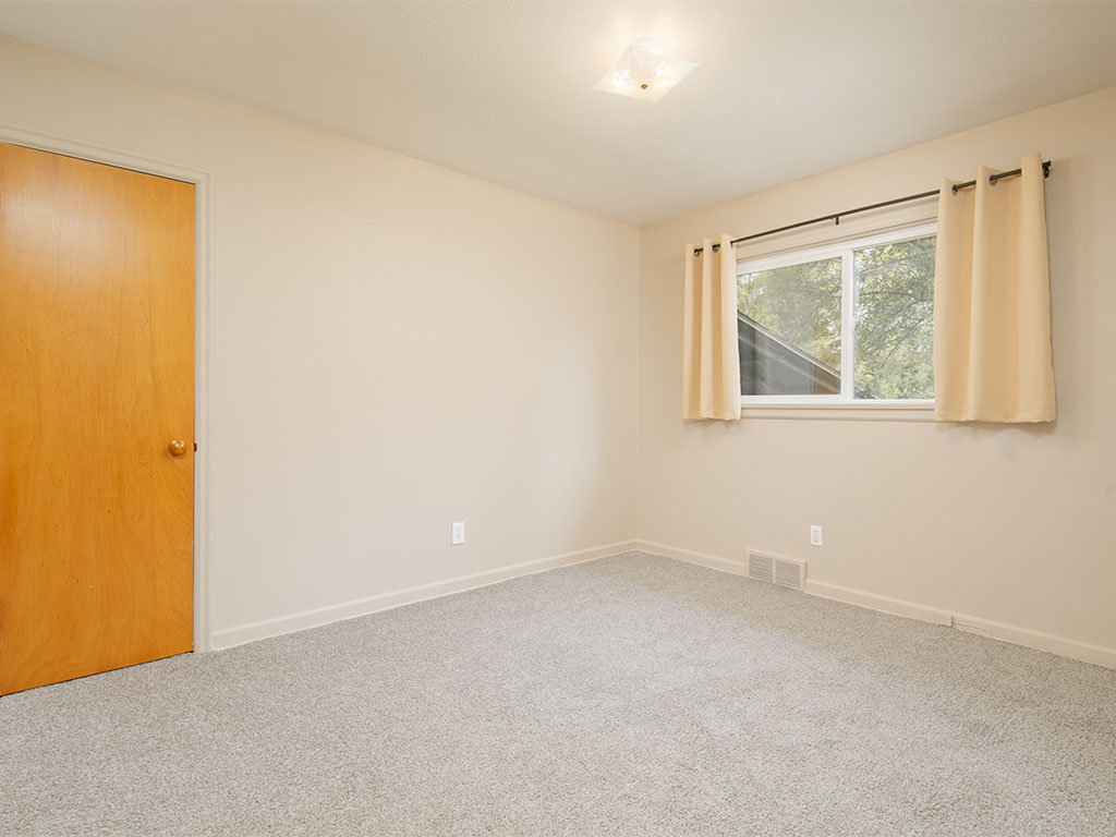 Empty carpeted room with a wooden door and a curtained window.