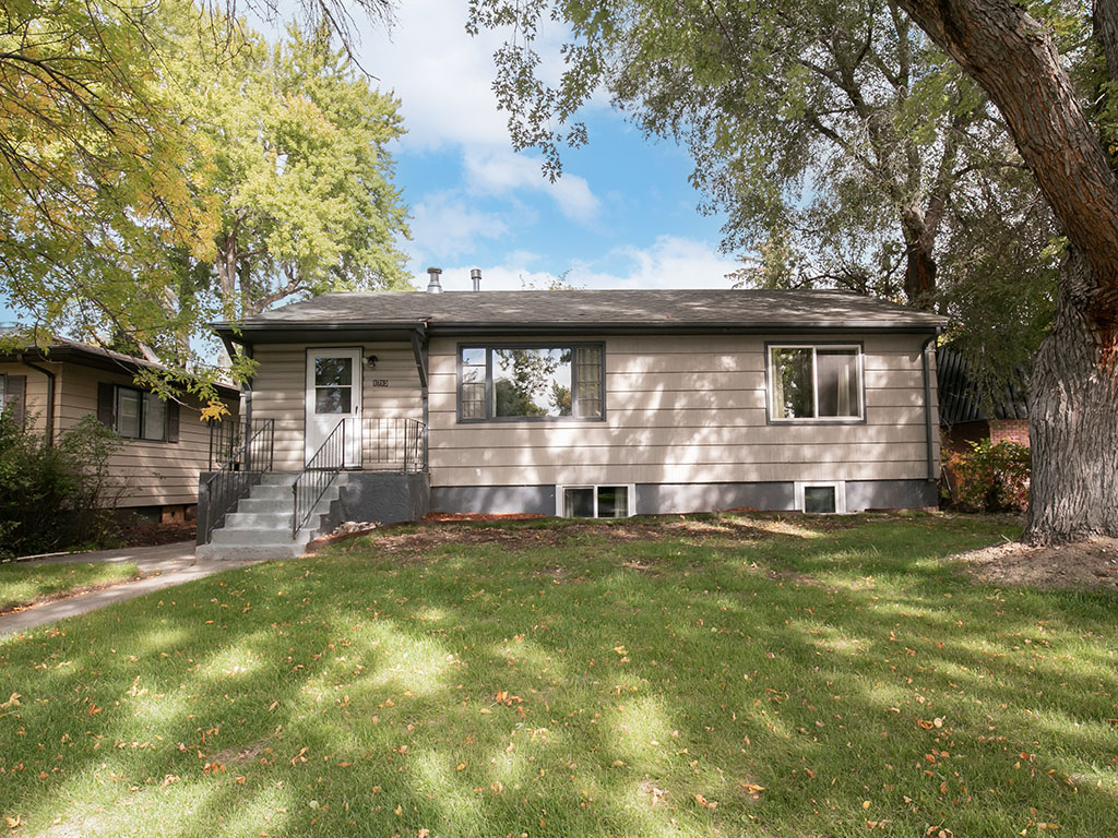 Single-story beige-sided home with a raised front porch and lawn beneath mature trees.