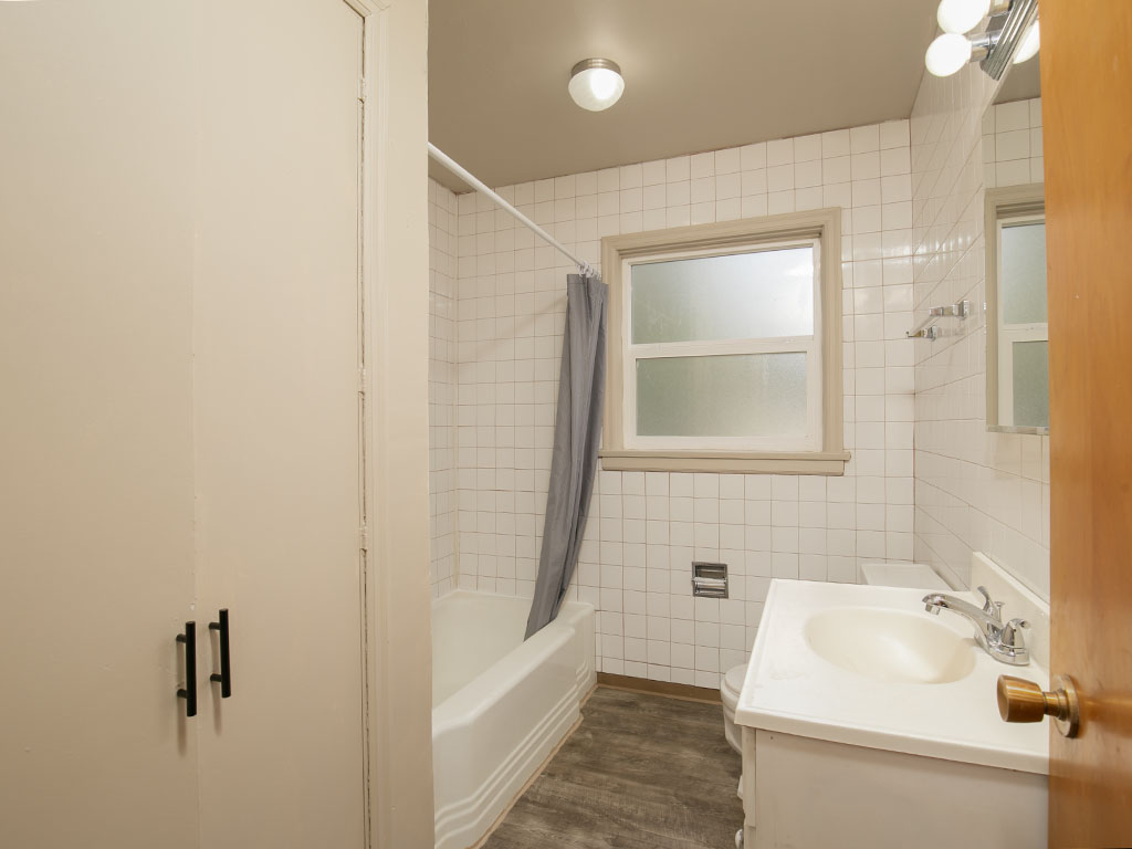 Bathroom with tiled walls, bathtub, frosted window, and white vanity.