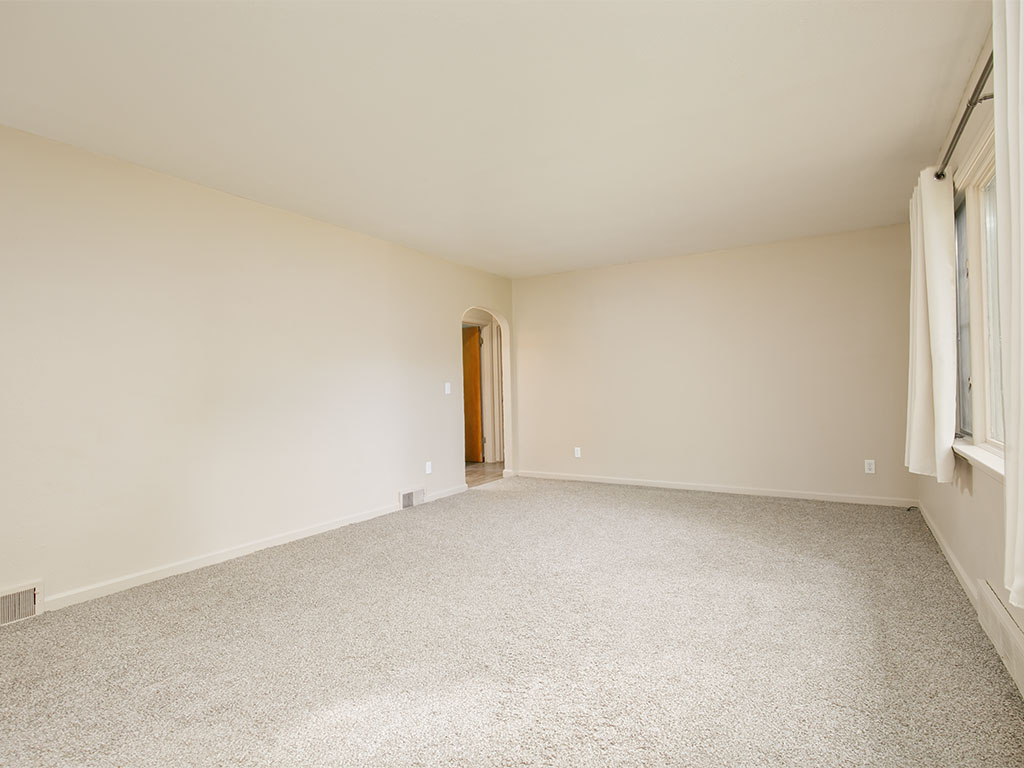 Empty living room with beige carpet, an arched doorway, and tall curtained windows.