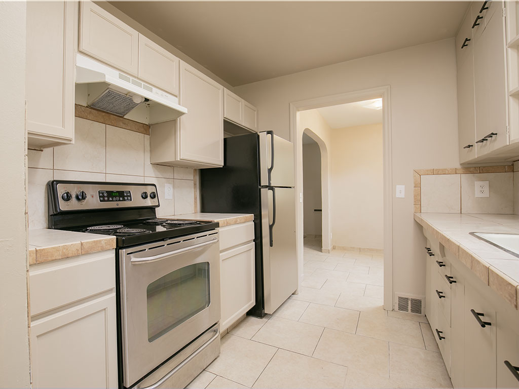 Galley kitchen with white cabinets, tiled counters, a stainless steel range, and a black-and-stainless refrigerator.