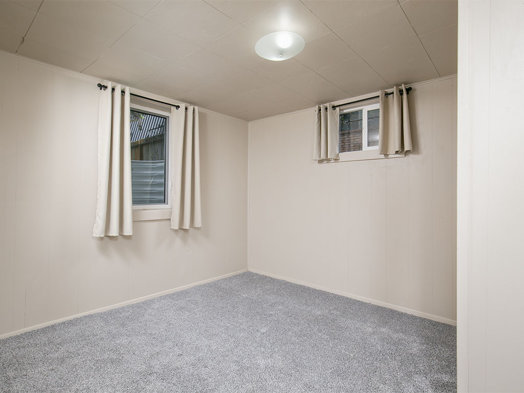 Empty carpeted room with two curtained windows and a low ceiling.