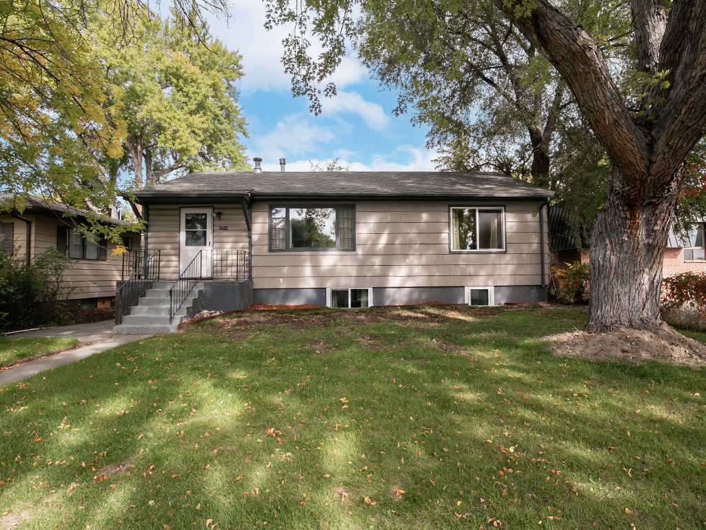 Single-story beige home with raised front steps, a broad lawn, and mature trees.