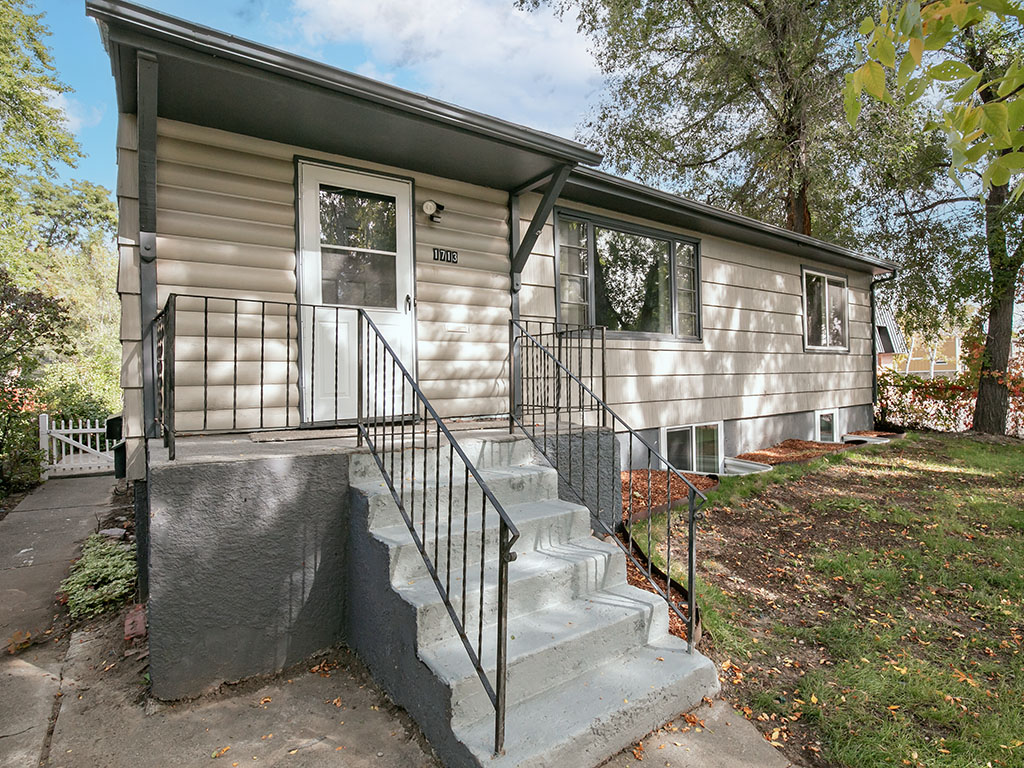 Single-story home with a raised front entry, concrete steps, black railings, and mature trees.