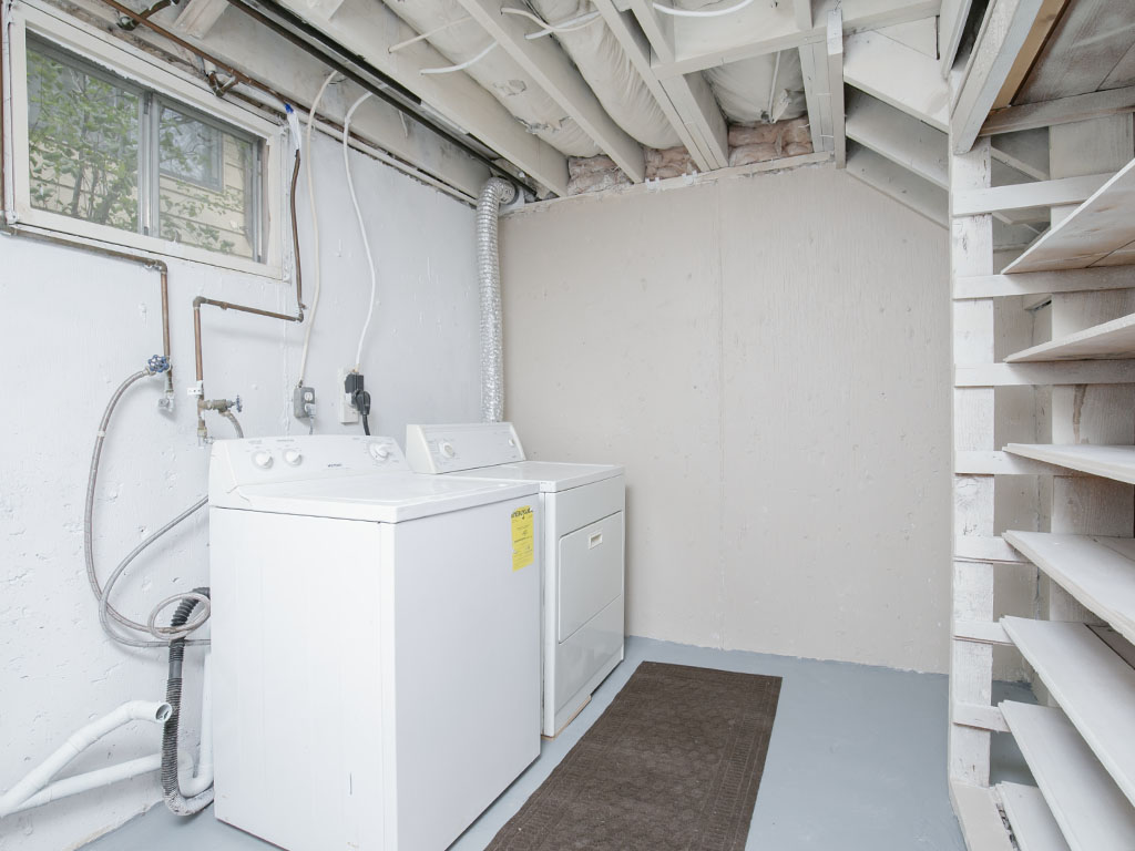 Basement laundry room with a white washer and dryer, exposed ceiling, and open shelving.