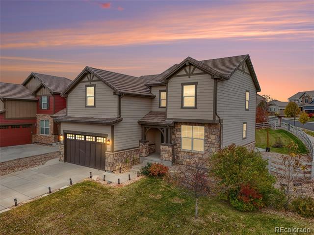 Two-story gray home with stone accents and a double garage beneath a pink dusk sky.