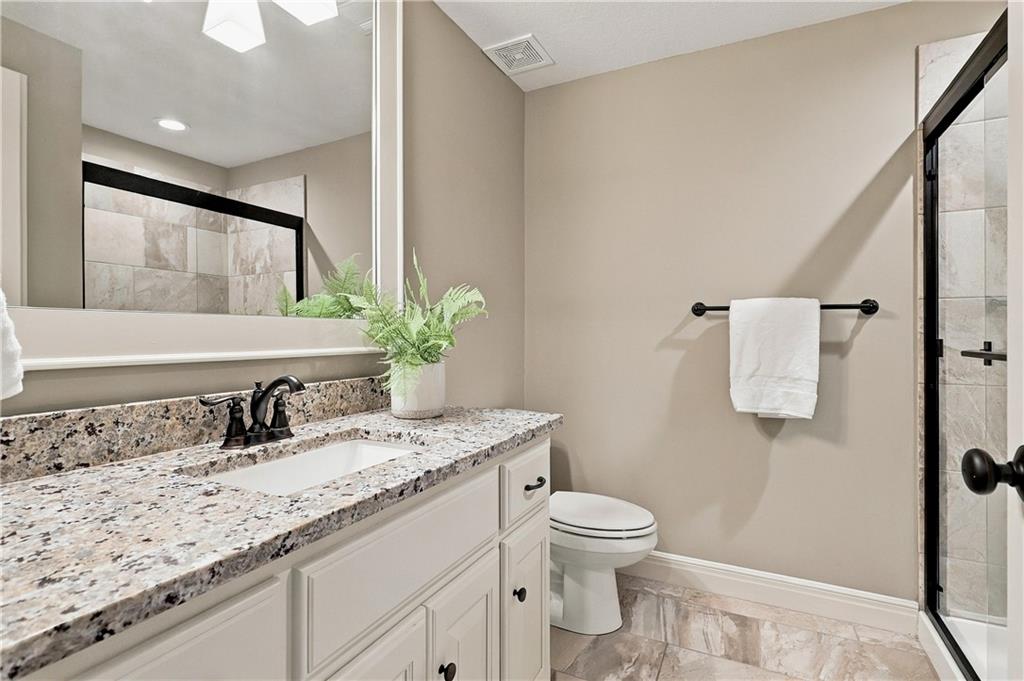 Bathroom with a granite vanity, large mirror, and black-framed glass shower.