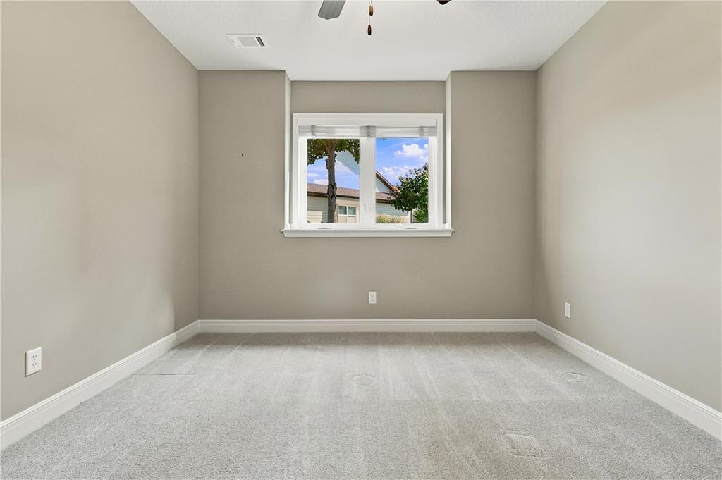 Empty bedroom with light carpet, gray walls, and a window facing a neighboring house.