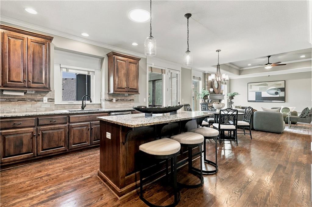 Open-plan kitchen with a granite island, dark wood cabinets, and breakfast stools adjoining the dining and living areas.