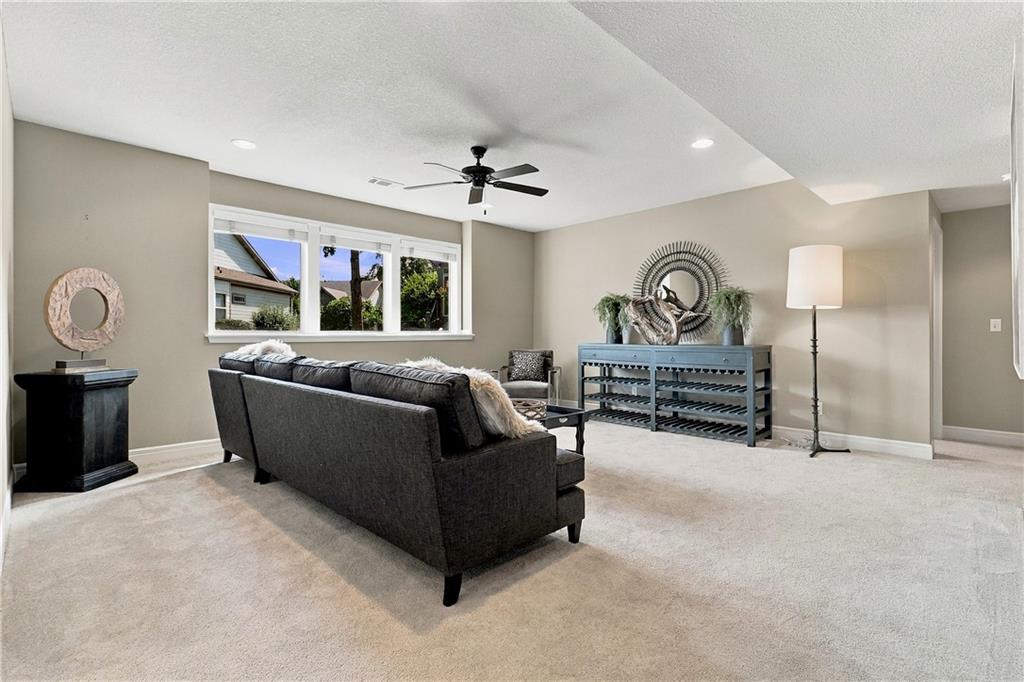 Furnished living room with a dark sectional sofa, wide window, and ceiling fan.