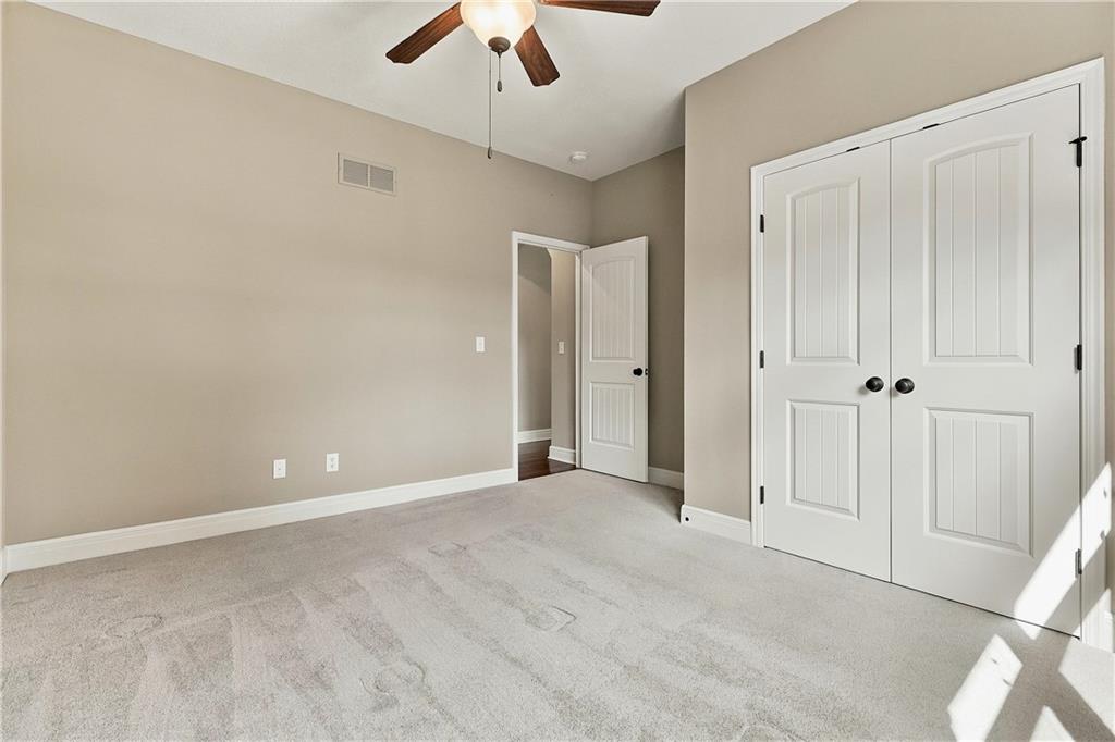 Vacant bedroom with white closet doors, light carpet, and a ceiling fan.