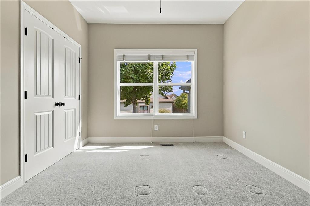 Empty bedroom with white closet doors and a window overlooking neighboring homes.