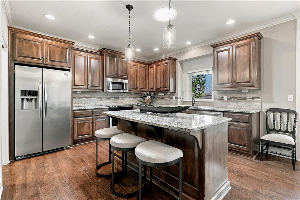 Kitchen with dark wood cabinets, stainless steel appliances, and a stone island with three stools.