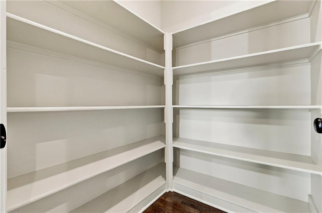 Walk-in pantry with white wraparound shelves and dark wood flooring.