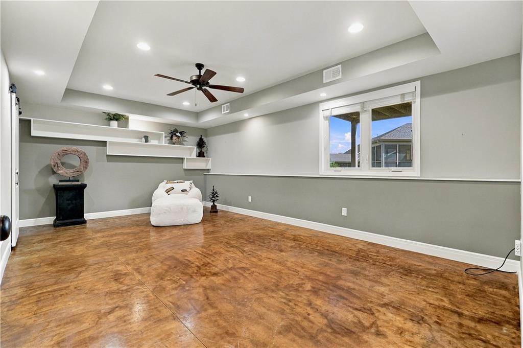 Living room with polished concrete flooring, floating shelves, and a ceiling fan.