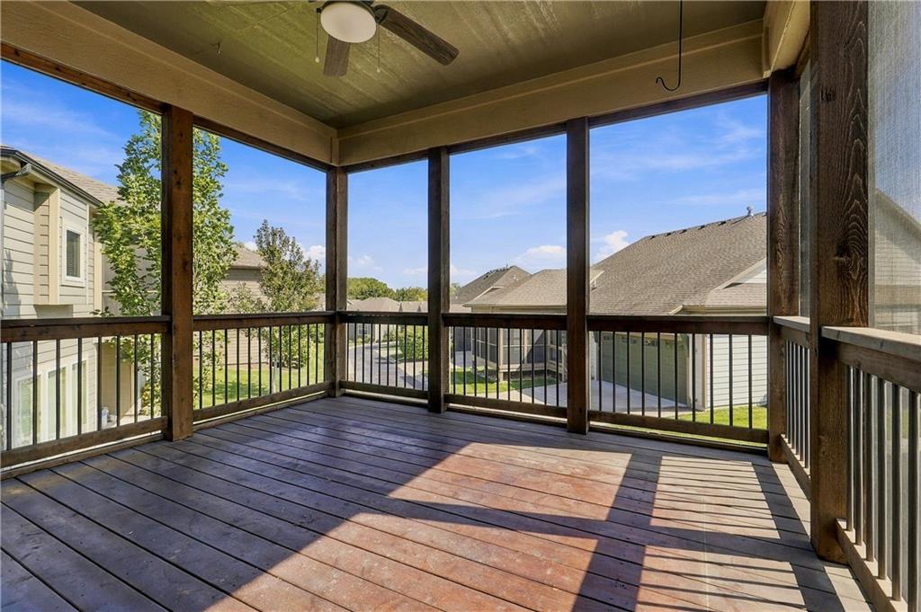 Screened porch with dark wood flooring, railings, and a ceiling fan overlooking neighboring homes.