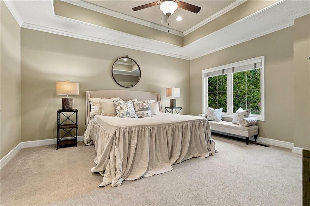 Staged bedroom with a large bed, tray ceiling, and window-seat bench.