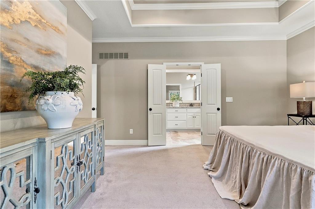 Staged bedroom with an ornate blue-gray cabinet and open doors leading to a bright bathroom.