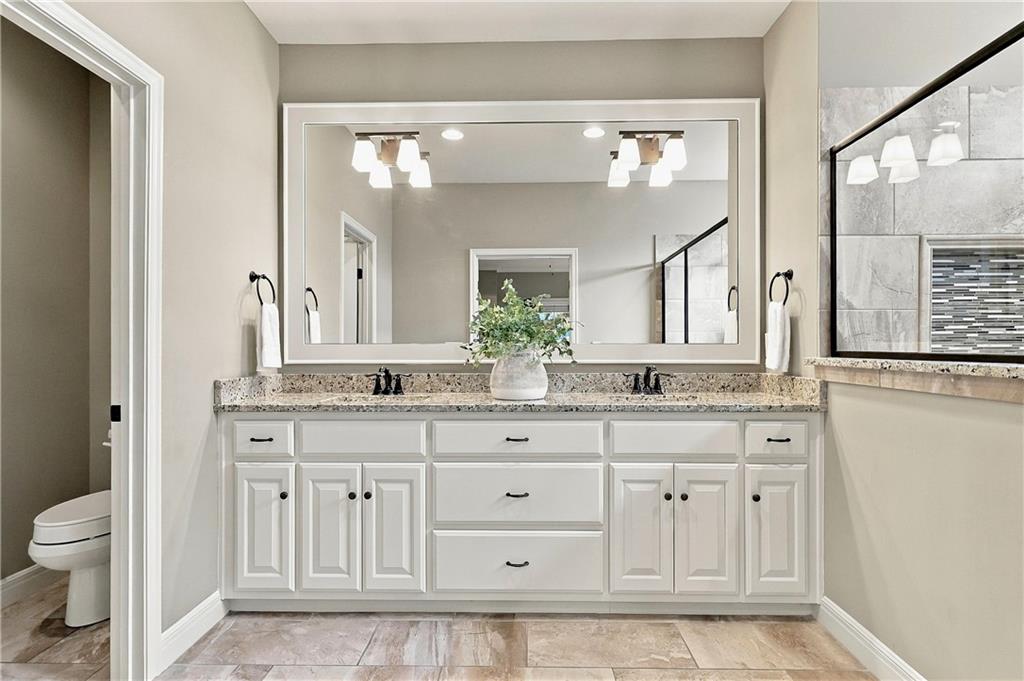 Bathroom with double-sink vanity, white cabinetry, stone countertop, and large framed mirror.