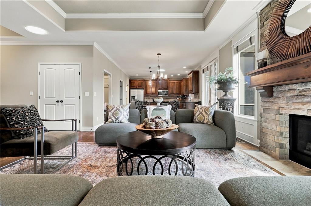 Furnished living room with a gray sectional, round coffee table, and stone fireplace; kitchen in the background.