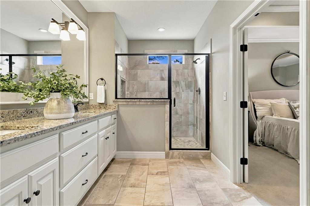 Bathroom with a long stone-topped vanity and a black-framed glass shower beside an open bedroom doorway.