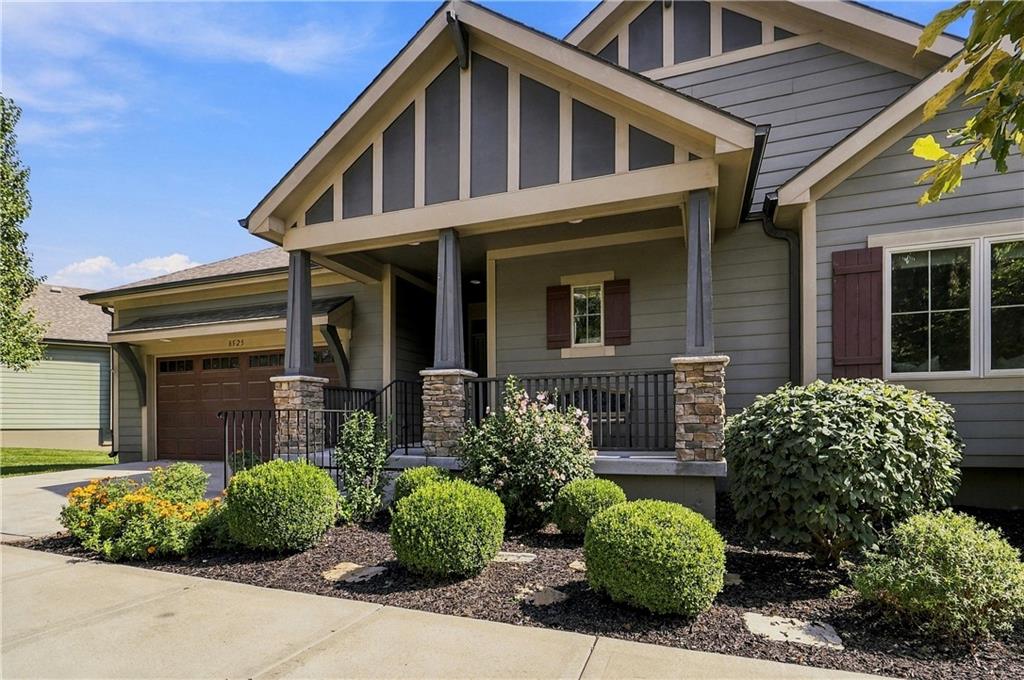 Gray Craftsman-style home with a gabled porch, stone column bases, and landscaped front garden.