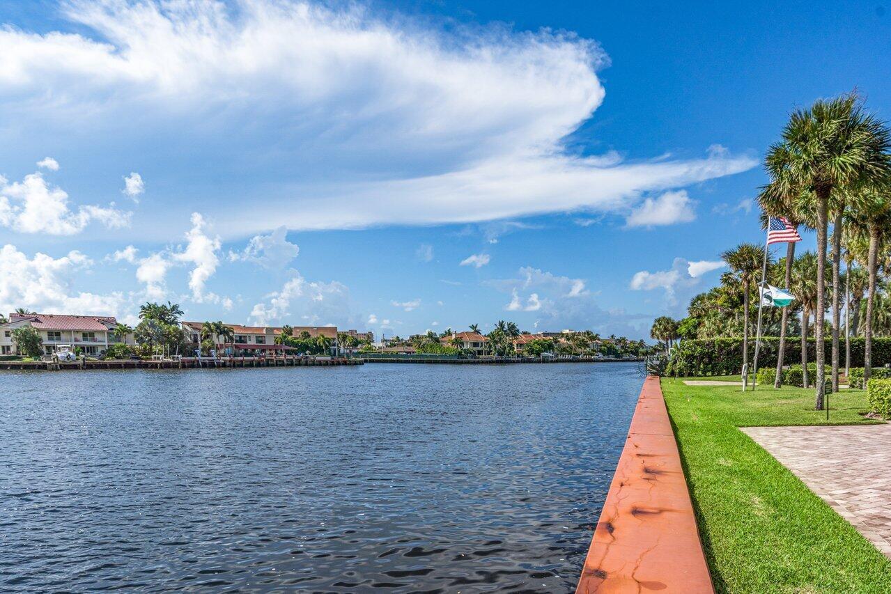 Canal view with waterfront homes, a red-orange seawall, palms, and lawn.