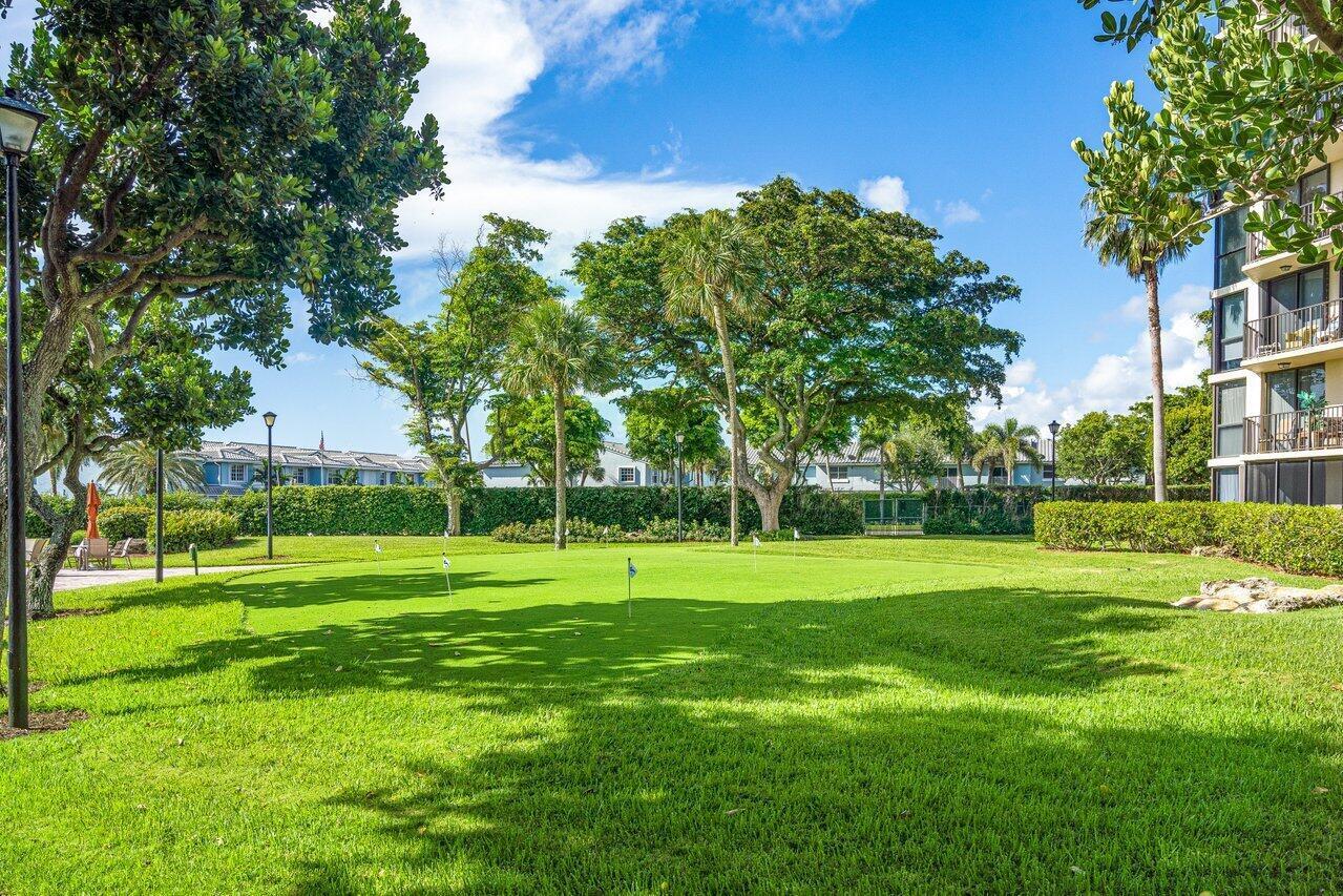 Landscaped putting green beside a condominium building, shaded by mature trees.