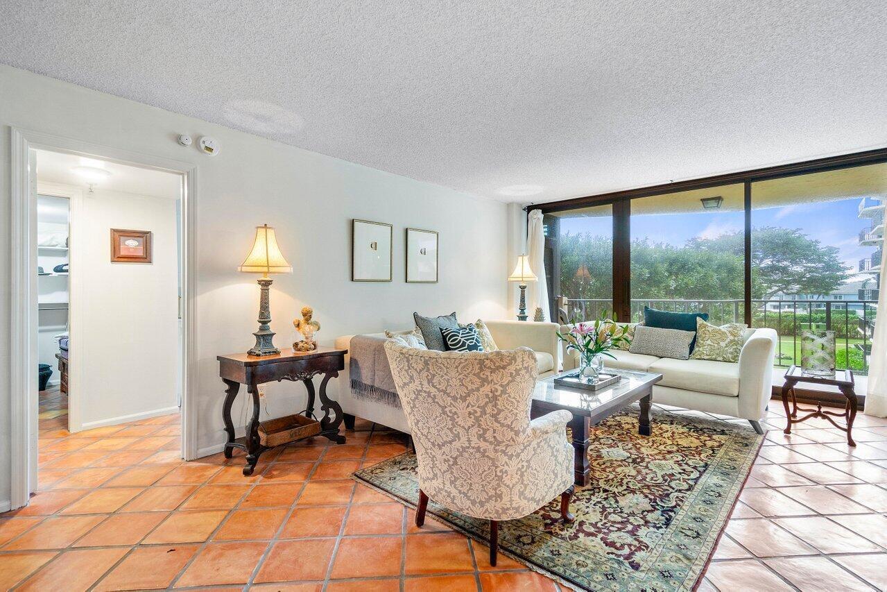 Furnished living room with terracotta tile floors, cream sofas, and sliding glass doors overlooking greenery.