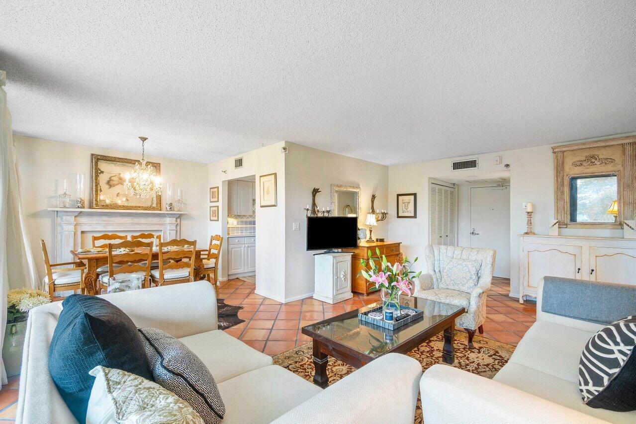 Open living and dining room with white sofas, terracotta tile floors, and a dining table beneath a chandelier.