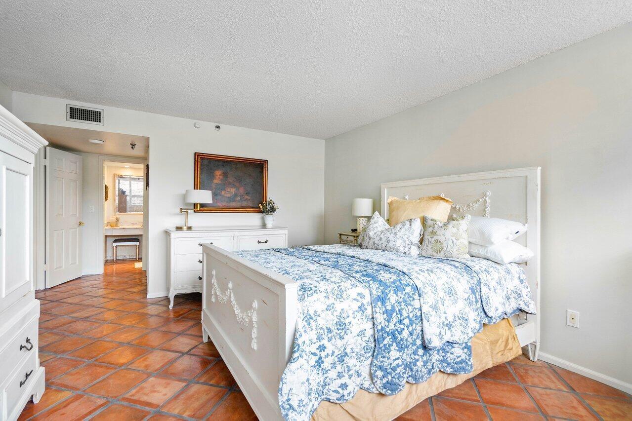 Bedroom with blue-and-white floral bedding, white furniture, and terracotta tile floors.