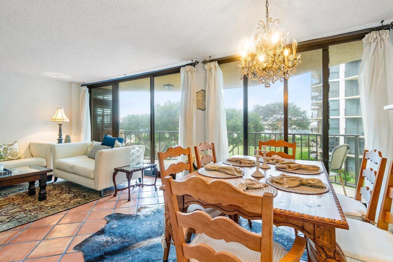 Condo dining area with a wooden table, chandelier, white sofa, and balcony windows overlooking trees.