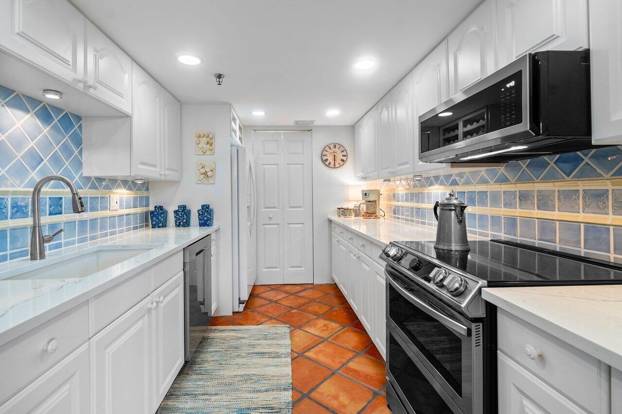 Kitchen with white cabinetry, blue patterned tile backsplash, stainless steel appliances, and terracotta flooring.