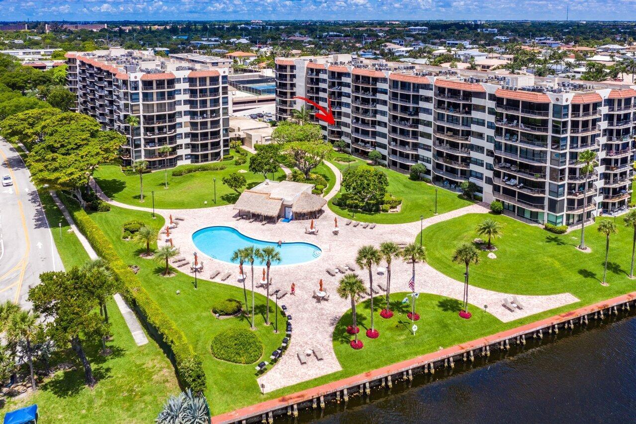Aerial view of waterfront condominium buildings, landscaped grounds, and a swimming pool.