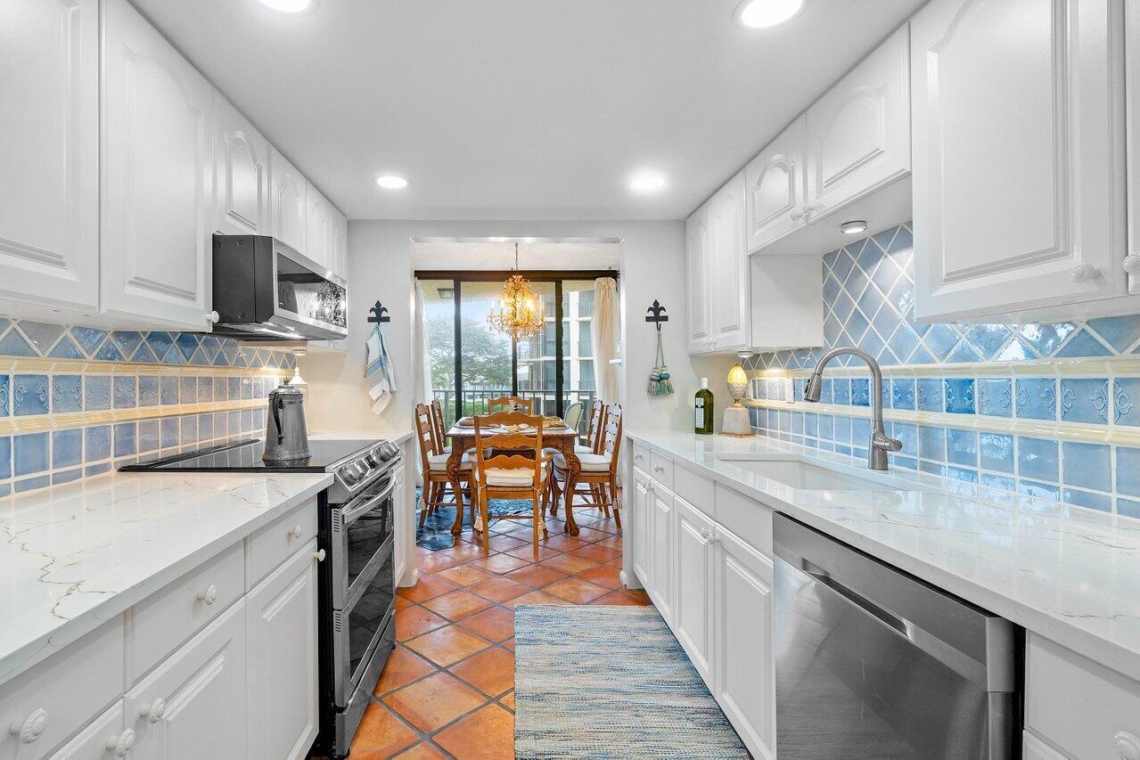 Bright white kitchen with blue tile backsplash, stainless steel appliances, and dining area by sliding glass doors.